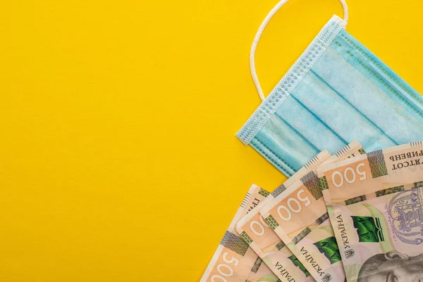 Вид украинских банкнот и медицинской маски на желтом фоне — стоковое фото