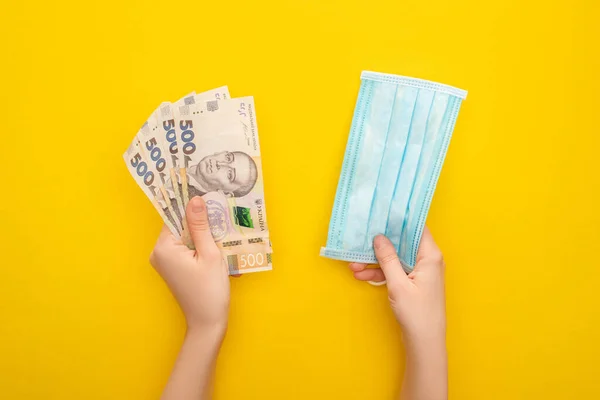 Partial view of woman holding Ukrainian banknotes and medical mask on yellow background — Stock Photo
