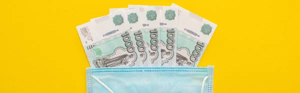 Vue du haut des billets russes et masque médical sur fond jaune, prise de vue panoramique — Photo de stock