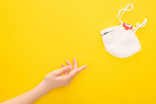 Partial view of woman pointing at safety mask on yellow background — Stock Photo