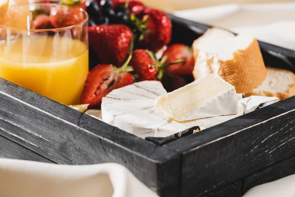 Vista de cerca del desayuno francés con Camembert, zumo de naranja, bayas y baguette en bandeja de madera - foto de stock