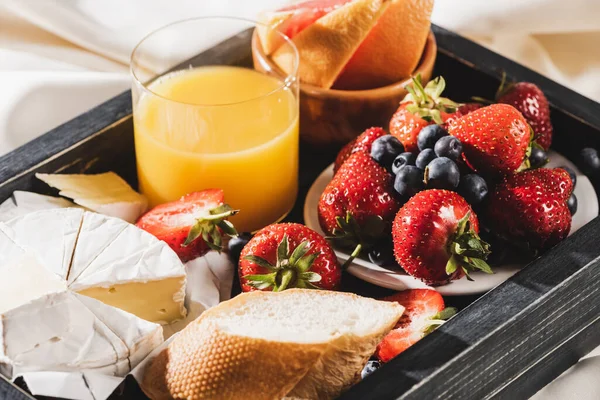 Close up view of french breakfast with grapefruit, Camembert, orange juice, berries and baguette on wooden tray — Stock Photo