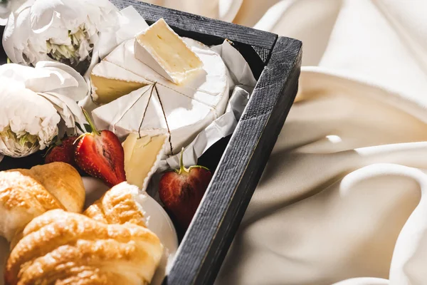 Vista de cerca del desayuno francés con croissant, Camembert, fresas en bandeja de madera sobre tela blanca texturizada con peonías - foto de stock