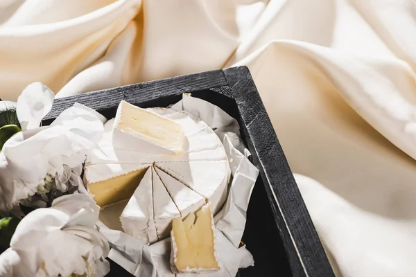 Vista da vicino della colazione alla francese con Camembert su vassoio di legno su panno bianco strutturato con peonie — Foto stock