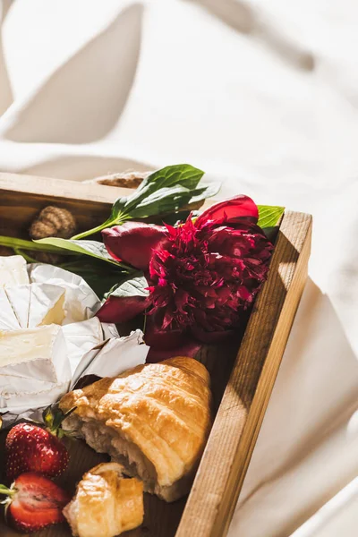 Vista de perto do café da manhã francês com croissant, Camembert, morangos em bandeja de madeira em pano branco texturizado com peônia — Fotografia de Stock