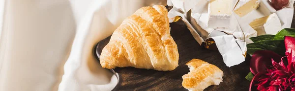 Vista superior del desayuno francés con croissant, Camembert, peonía sobre tabla de cortar de madera sobre mantel blanco, plano panorámico - foto de stock