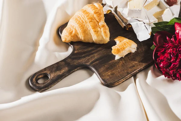 Vue du haut du petit déjeuner français avec croissant, camembert, pivoine sur planche à découper en bois sur nappe blanche — Photo de stock