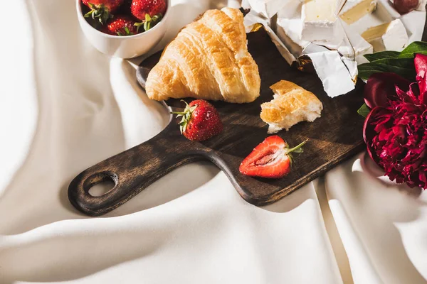 Top view of french breakfast with strawberries, croissant, Camembert, peony on wooden cutting board on white tablecloth — Stock Photo