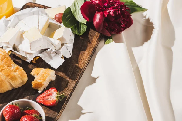 Französisches Frühstück mit Erdbeeren, Croissant, Camembert, Pfingstrose auf Holzschneidebrett auf weißer Tischdecke — Stockfoto