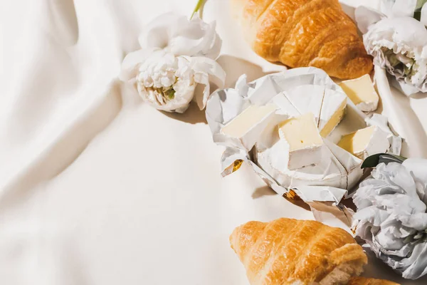 Blick von oben auf französisches Frühstück mit Croissants, Camembert, Pfingstrosen auf weißer Tischdecke — Stockfoto