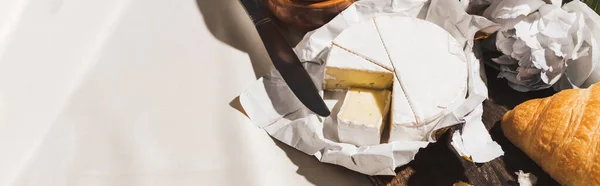 Draufsicht auf französisches Frühstück mit Croissant, Camembert, Pfingstrose auf Holzschneidebrett auf weißer Tischdecke, Panoramaaufnahme — Stockfoto