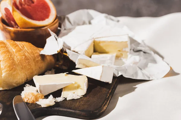 Selective focus of french breakfast with croissant, Camembert, grapefruit on wooden cutting board on white tablecloth — Stock Photo