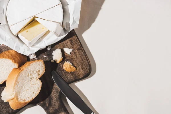 Vista superior do café da manhã francês com baguete, Camembert, faca na placa de corte de madeira na toalha de mesa branca — Fotografia de Stock