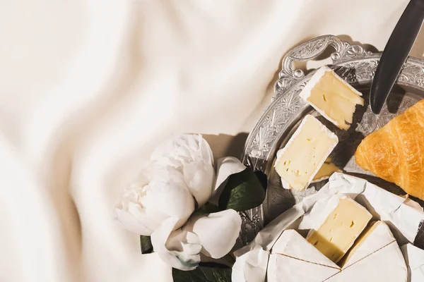 Vista dall'alto della colazione francese con croissant, Camembert, peonia e coltello su vassoio d'argento su tovaglia bianca — Foto stock