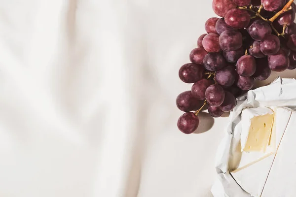 Draufsicht auf französisches Frühstück mit Trauben und Camembert auf texturierter weißer Tischdecke — Stockfoto