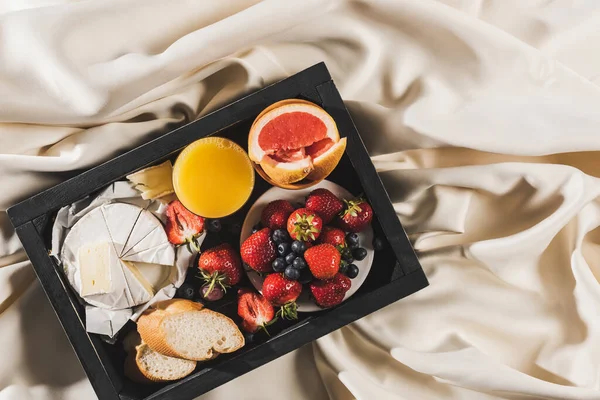 Vista superior do café da manhã francês com toranja, Camembert, suco de laranja, bagas e baguete na bandeja na toalha de mesa branca — Fotografia de Stock