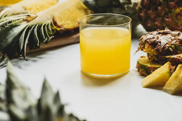 Selektiver Fokus von frischem Ananassaft in der Nähe von geschnittenen köstlichen Früchten auf weißem Hintergrund — Stockfoto