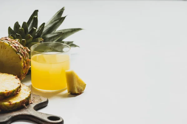 Свежий ананасовый сок рядом сократить вкусные фрукты на деревянной доске резки на белом фоне — стоковое фото