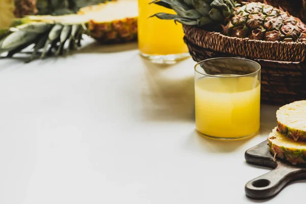 Вибірковий фокус свіжого ананасового соку в склянці біля смачних фруктів в кошику на білій поверхні — стокове фото