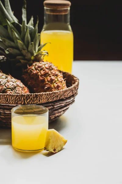 Enfoque selectivo de jugo de piña fresca en vidrio y botella cerca de deliciosa fruta en cesta sobre fondo blanco aislado en negro - foto de stock