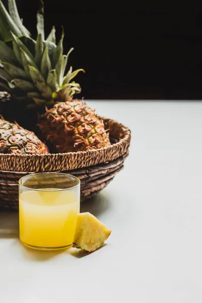 Jus d'ananas frais près de délicieux fruits dans le panier sur fond blanc isolé sur fond noir — Photo de stock