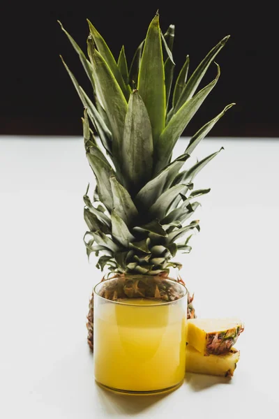 Succo d'ananas fresco in vetro vicino tagliato delizioso frutto su superficie bianca isolato su nero — Foto stock