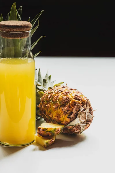Fresh pineapple juice in bottle near cut delicious fruit on white surface isolated on black — Stock Photo