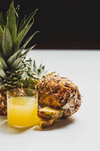 Fresh pineapple juice near cut delicious fruit on white surface isolated on black — Stock Photo