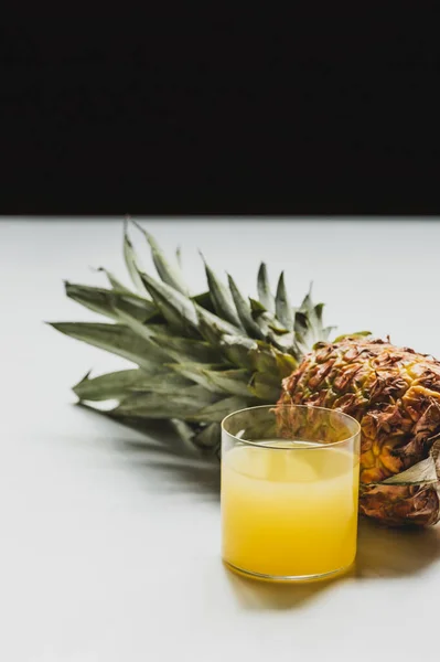 Свежий ананасовый сок рядом сократить вкусные фрукты на белой поверхности изолированы на черном — стоковое фото