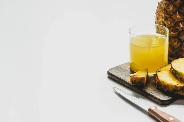 Fresh pineapple juice in glass near cut delicious fruit on wooden cutting board with knife on white background — Stock Photo