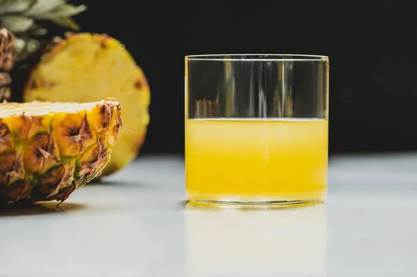 Messa a fuoco selettiva di succo d'ananas fresco e tagliare deliziosi frutti sulla superficie bianca su sfondo nero — Foto stock