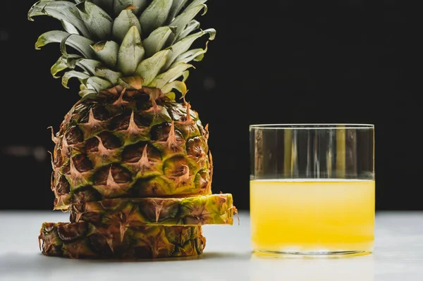 Suco de abacaxi fresco e cortar frutas deliciosas na superfície branca no fundo preto — Fotografia de Stock