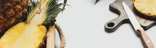 Вибірковий фокус свіжого розрізаного ананаса на дерев'яному підносі та обробній дошці з ножем на білому тлі, панорамна орієнтація — стокове фото