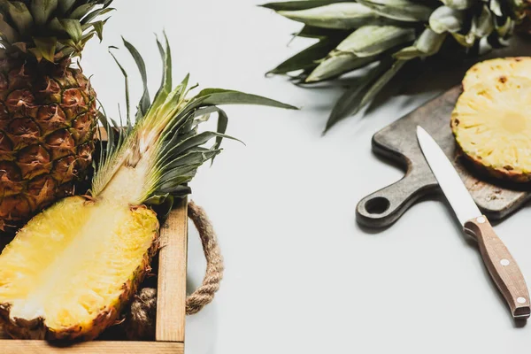 Селективный фокус свежевырезанного ананаса на деревянном подносе и разделочной доске с ножом на белом фоне — стоковое фото
