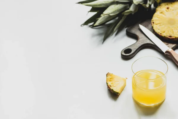 Foyer sélectif de jus d'ananas frais près de fruits délicieux coupés sur planche à découper avec couteau sur fond blanc — Photo de stock
