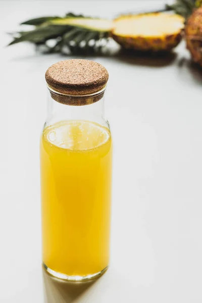 Selective focus of fresh pineapple juice in bottle near cut delicious fruit on white background — Stock Photo