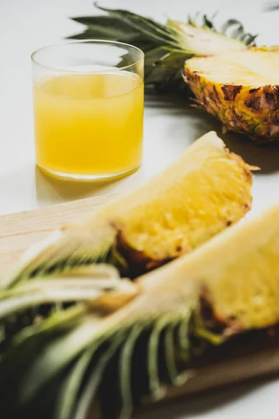 Foco seletivo de suco de abacaxi fresco perto de cortar frutas deliciosas na placa de corte no fundo branco — Fotografia de Stock