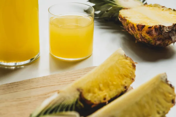 Foyer sélectif de jus d'ananas frais en bouteille et en verre près de fruits délicieux coupés sur planche à découper sur fond blanc — Photo de stock