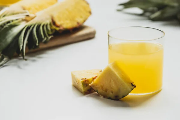 Вибірковий фокус свіжого ананасового соку біля нарізаних смачних фруктів на обробній дошці на білому тлі — стокове фото