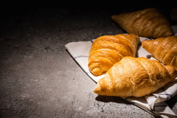 Croissant appena sfornati su asciugamano su superficie grigio cemento al buio — Foto stock