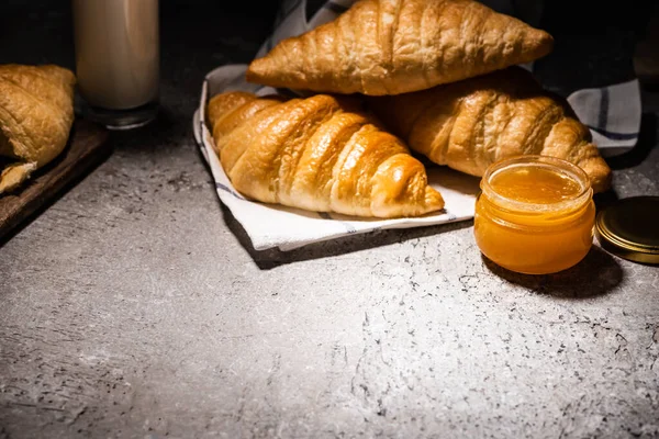 Croissants frais cuits au four sur la serviette près de la confiture sur la surface gris béton dans l'obscurité — Photo de stock