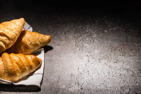 Croissant appena sfornati su asciugamano su superficie grigio cemento al buio — Foto stock