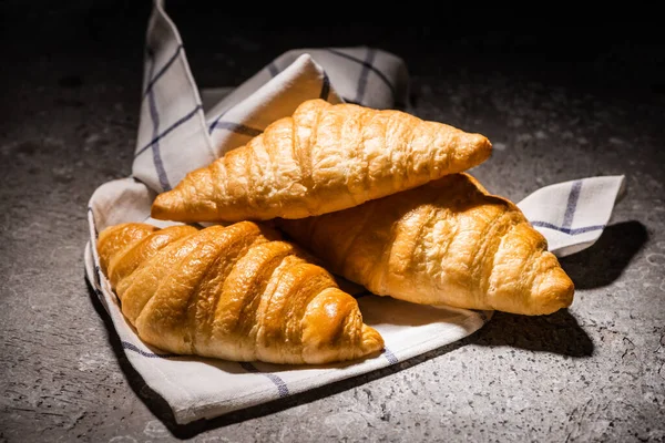 Fresh baked croissants on towel on concrete grey surface in dark — Stock Photo