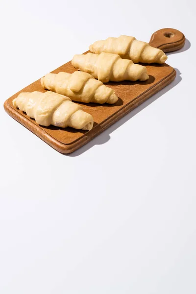 Croissants crus na placa de corte de madeira no fundo branco — Fotografia de Stock