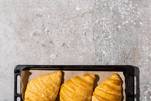 Vista superior de croissants deliciosos assados na bandeja de cozimento na superfície cinza concreta — Fotografia de Stock