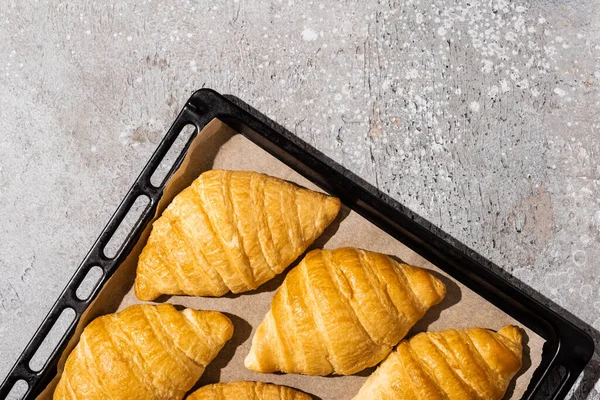 Vista superior de croissants deliciosos assados na bandeja de cozimento na superfície cinza concreta — Fotografia de Stock