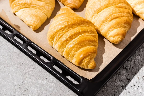 Baked delicious croissants on baking tray on concrete grey surface — Stock Photo