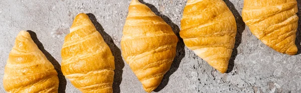 Pose plate avec des croissants frais cuits au four sur une surface gris béton, plan panoramique — Photo de stock