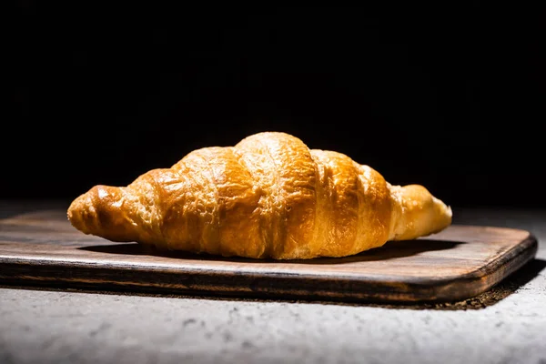Croissant cozido no forno fresco na placa de corte de madeira na superfície cinzenta concreta isolada no preto — Fotografia de Stock