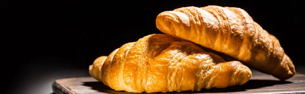 Fresh baked croissants on wooden cutting board isolated on black, panoramic shot — Stock Photo